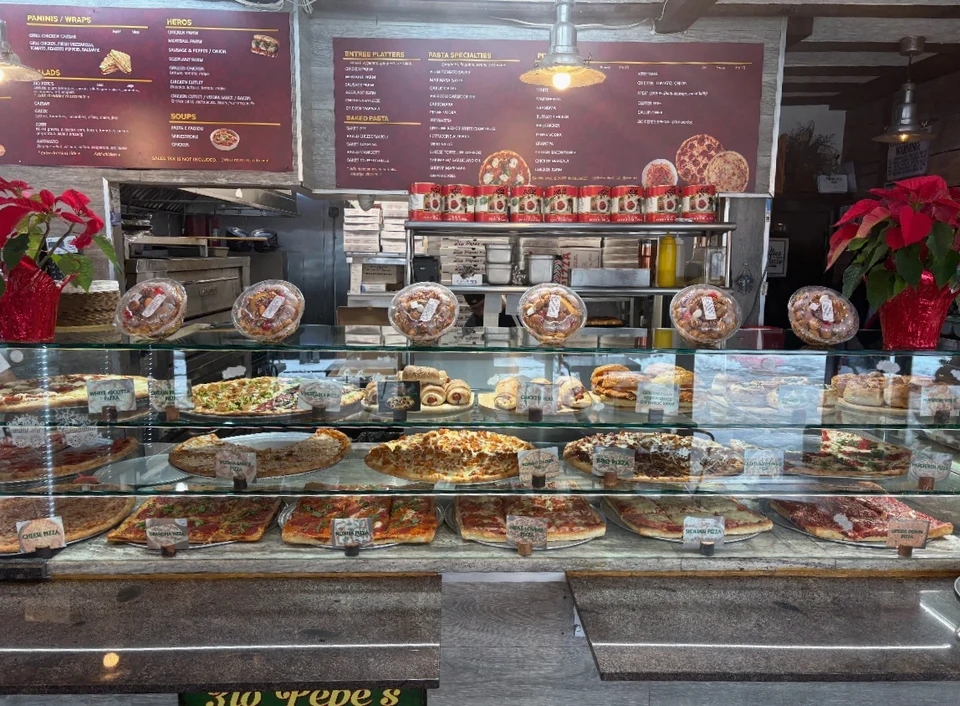 Pizza pies and rolls in Zio Pepe’s glass display, with the red menu boards behind the counter